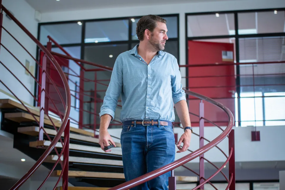 Dans les bureaux de Fame, un homme en chemise au pied de l'escalier en colimaçon.