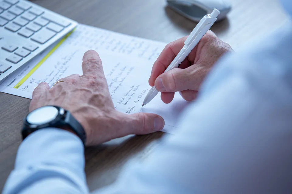Gros plan sur une main qui prend des notes au stylo, à côté d'un clavier.