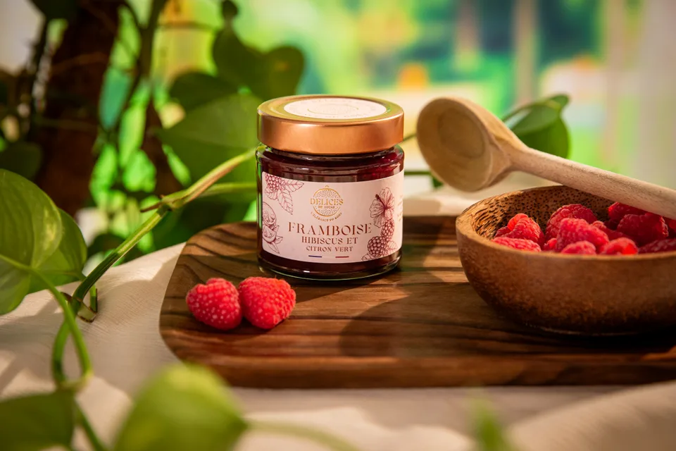 Un pot de confiture de framboise sur une planche, devant une coupelle de framboises fraîches.