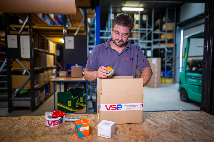 Dans l’entrepôt de VSPièces, un membre de l’équipe prépare une commande dans un carton aux couleurs de la marque. Zetruc accompagne la boutique en ligne depuis 2018.