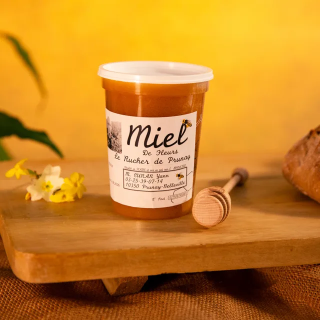 Un pot de miel local posé sur une planche, sur fond jaune.
