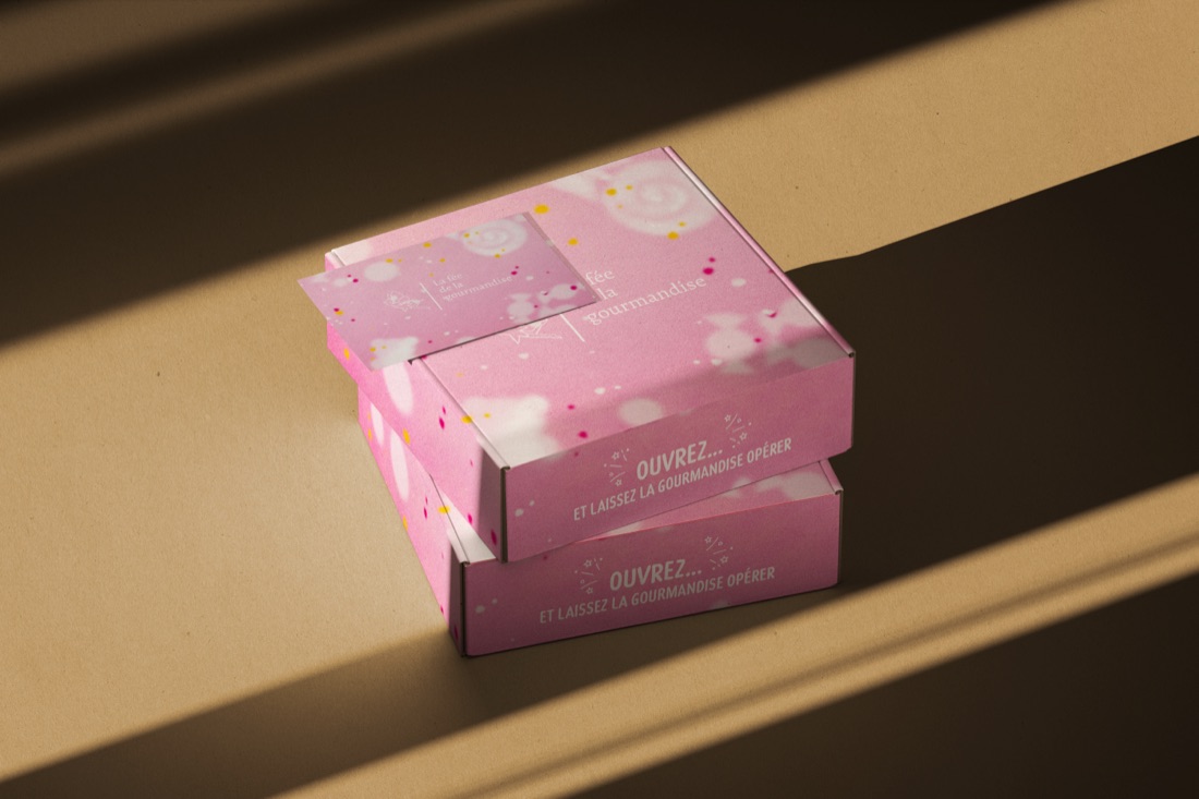 Deux coffrets roses de La Fée de la Gourmandise empilés, portant la mention « Ouvrez et laissez la gourmandise opérer ».