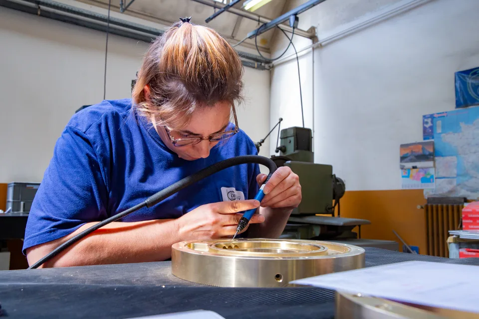 Concentrée, une technicienne de Degoisey travaille une pièce en laiton à l'outil rotatif.