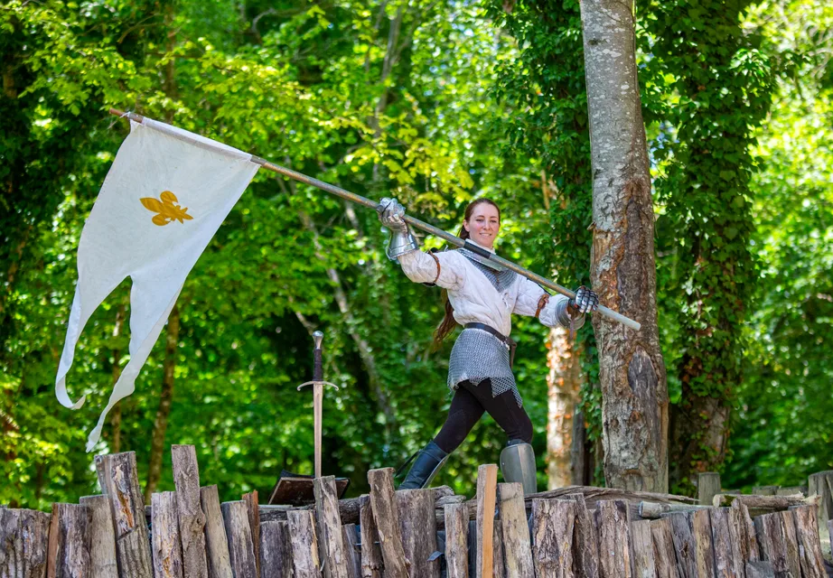Une comédienne incarne Jeanne d'Arc, bannière fleurdelisée à la main, pendant un spectacle de Grinyland.