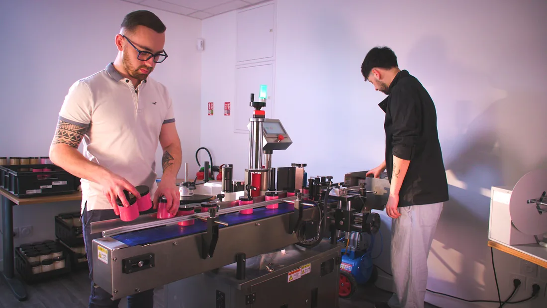 Dans l'atelier de La Fée de la Gourmandise, deux personnes à la ligne de conditionnement des pots roses.
