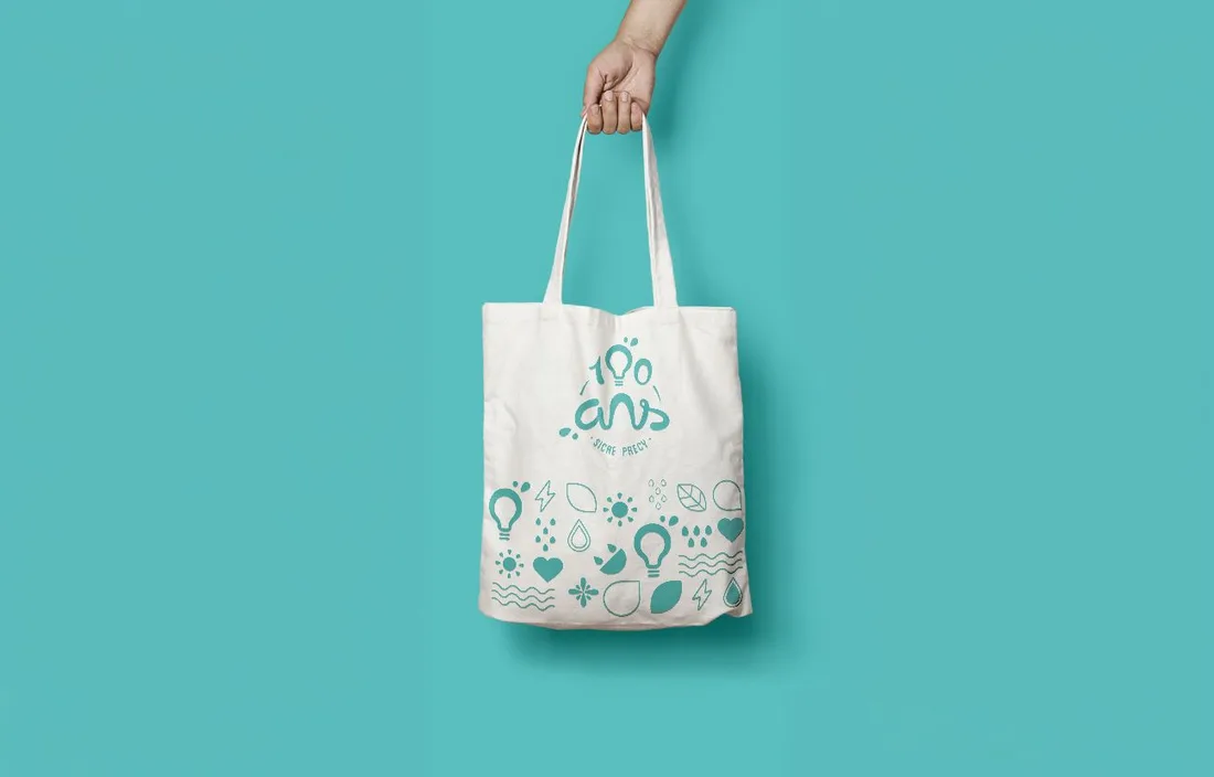 Un tote bag SICAE « 100 ans » imprimé en bleu, tenu à bout de bras.