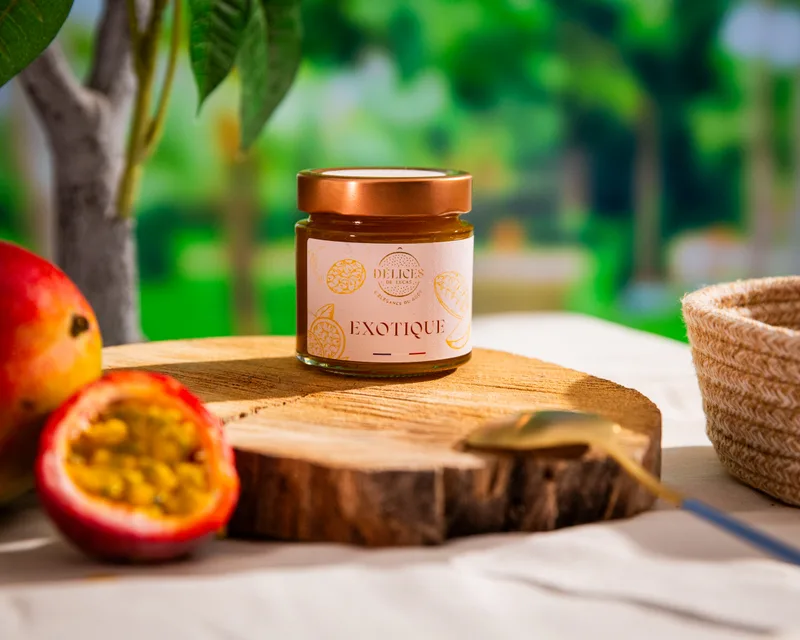 Un pot de confiture de fruits exotiques posé sur un rondin, entouré de fruits de la passion et de mangue.
