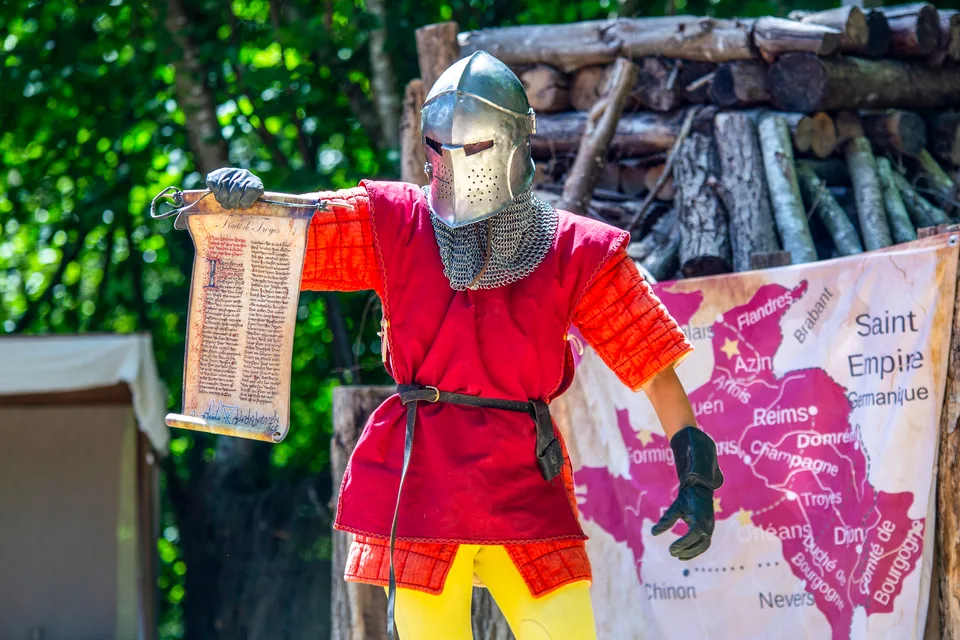 Un chevalier en armure déroule un parchemin devant une carte de la Champagne, pendant un spectacle de Grinyland.