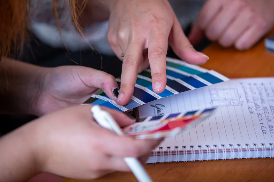 Des mains parcourent un nuancier de couleurs posé sur un carnet de notes.
