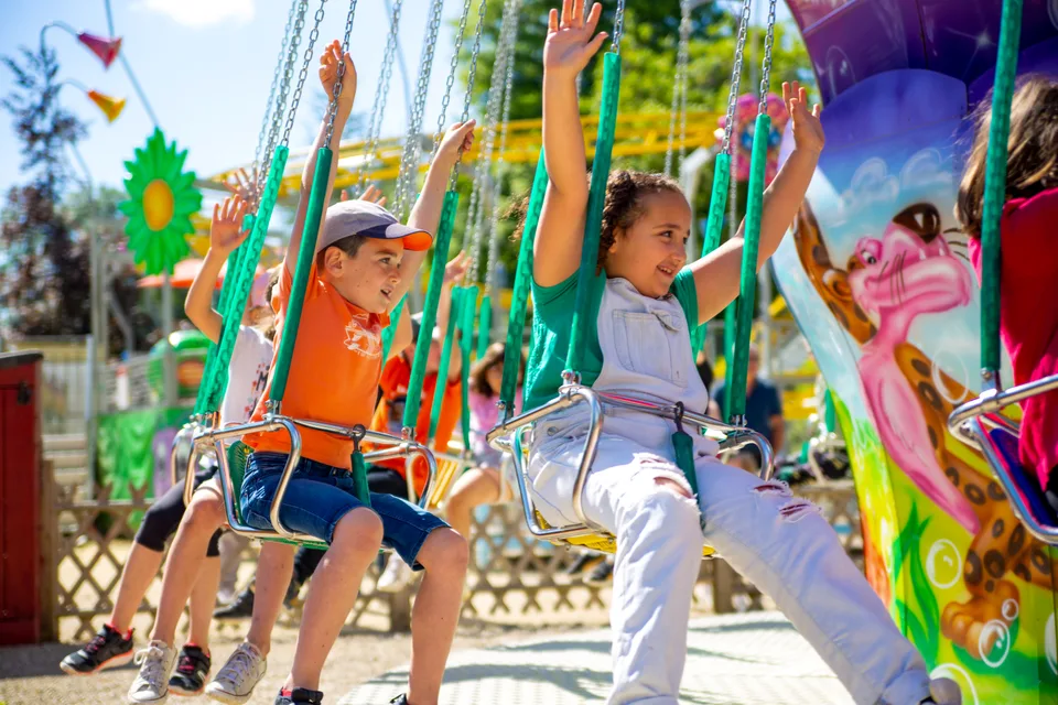 Des enfants, bras en l'air, s'amusent sur les chaises volantes du manège de Grinyland.