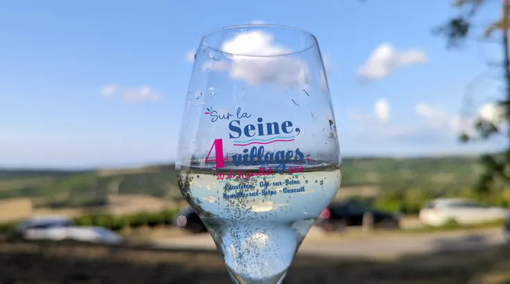 La flûte collector de l'édition 2024, « Sur la Seine, 4 villages », tenue devant le vignoble.
