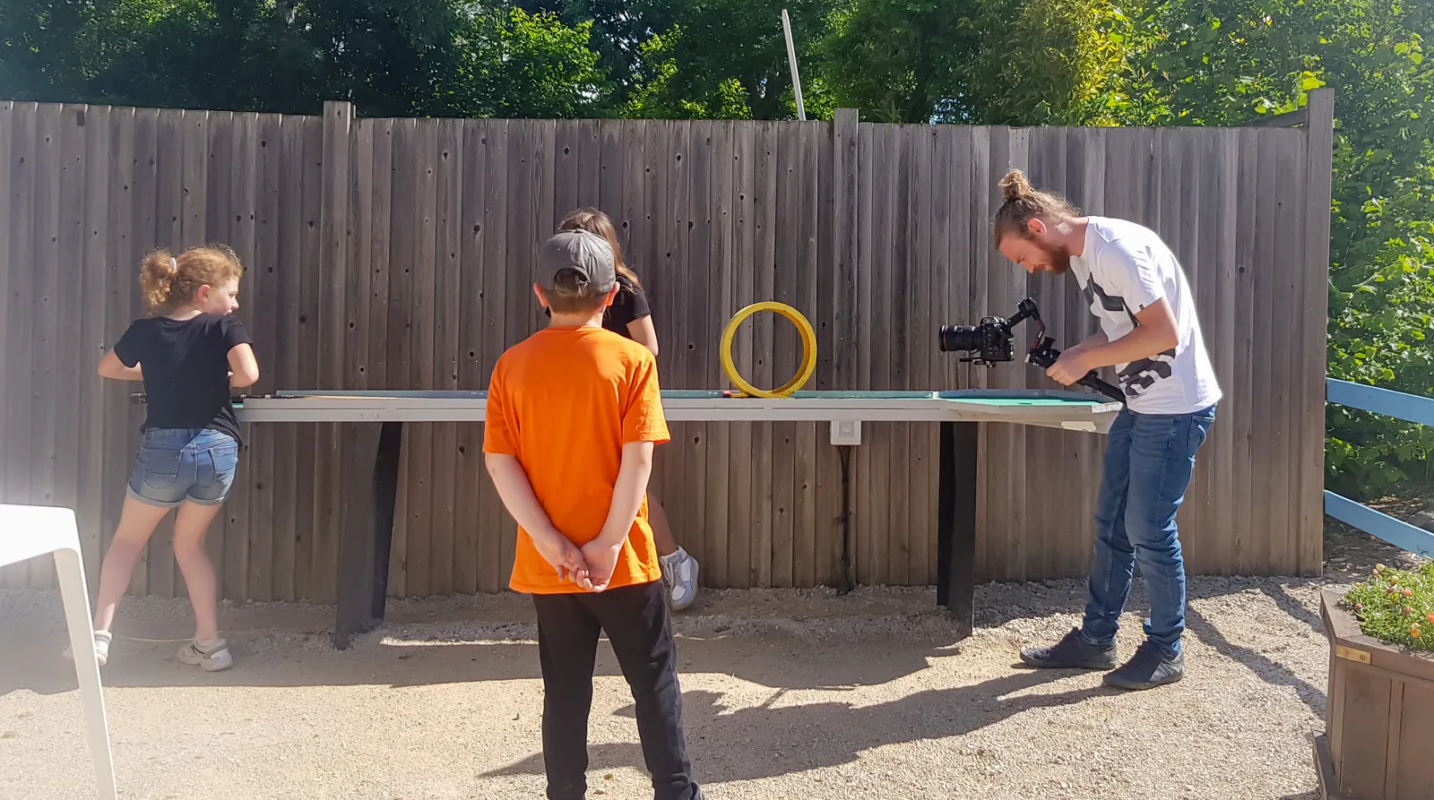 Un vidéaste de l'agence filme des enfants pendant un jeu d'adresse en extérieur.